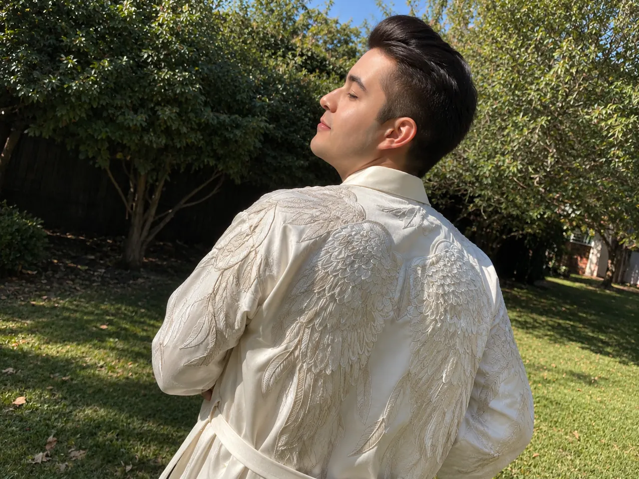 Igor Davis in an angel-wing embroidered robe, eyes closed in the sunlight of a garden
